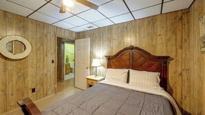 A bedroom with a wooden paneled wall, a bed with a wooden headboard, a nightstand with a lamp, and a ceiling fan.