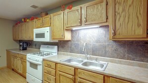 A kitchen with wooden cabinets, a white stove, a microwave, and a stainless steel sink.