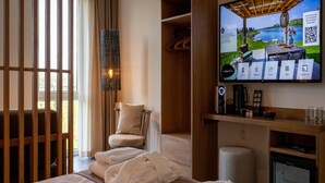 Ein Hotelzimmer mit Bett, Sessel, Fernseher und einer Minibar.