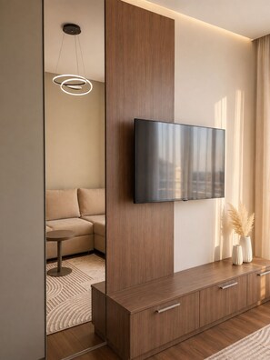 A modern living room with a flat-screen TV mounted on a wooden cabinet, a sofa, and a small round table. - Guest House Fjola : Family Two-Bedroom Apartment with View (Donji Štoj)