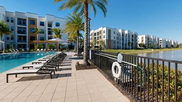A poolside area with lounge chairs, a lifebuoy, and a railing overlooking a body of water.