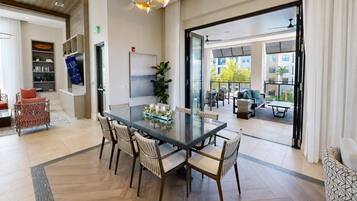 A modern dining area with a glass table, six chairs, and a large window offering a view of the outdoors.