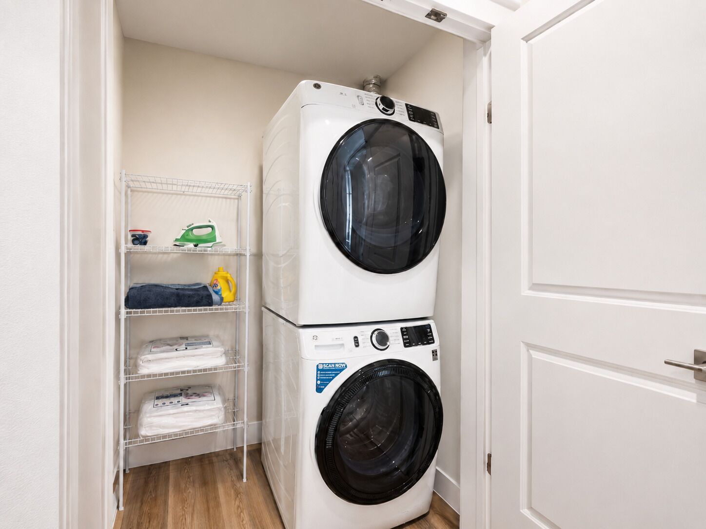 A laundry room with a stacked washer and dryer, shelves with folded clothes, and laundry supplies.