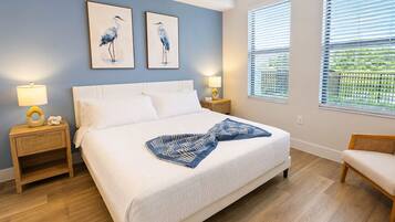A bedroom with a large bed, two bedside tables, a nightstand, a window with blinds, and two wall-mounted paintings of birds.