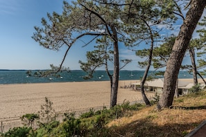 Una playa con una cerca de madera, árboles y un edificio con techo al fondo.