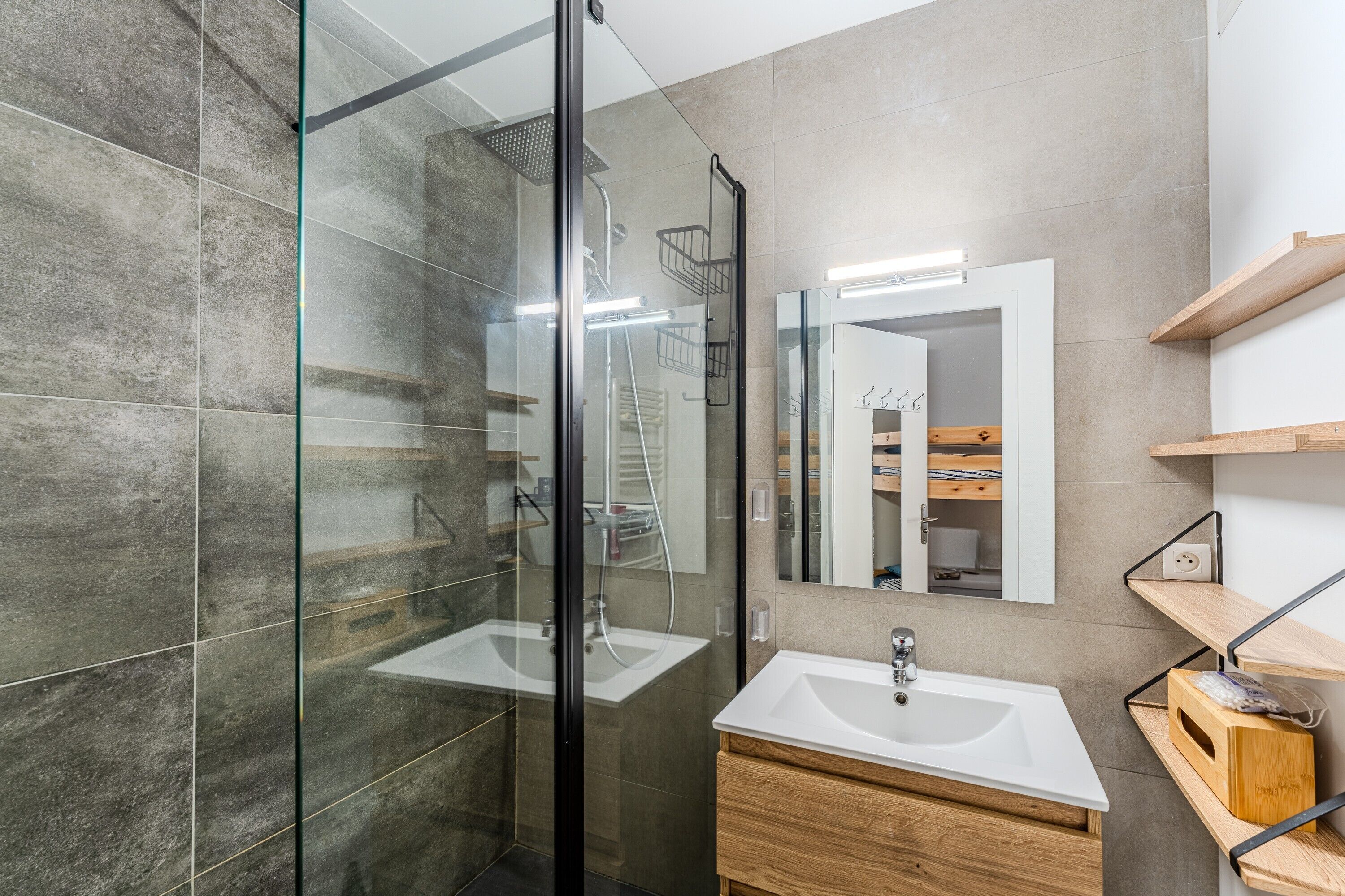 Un baño moderno con cabina de ducha de vidrio, lavamanos blanco, tocador de madera y espejo con marco de madera.