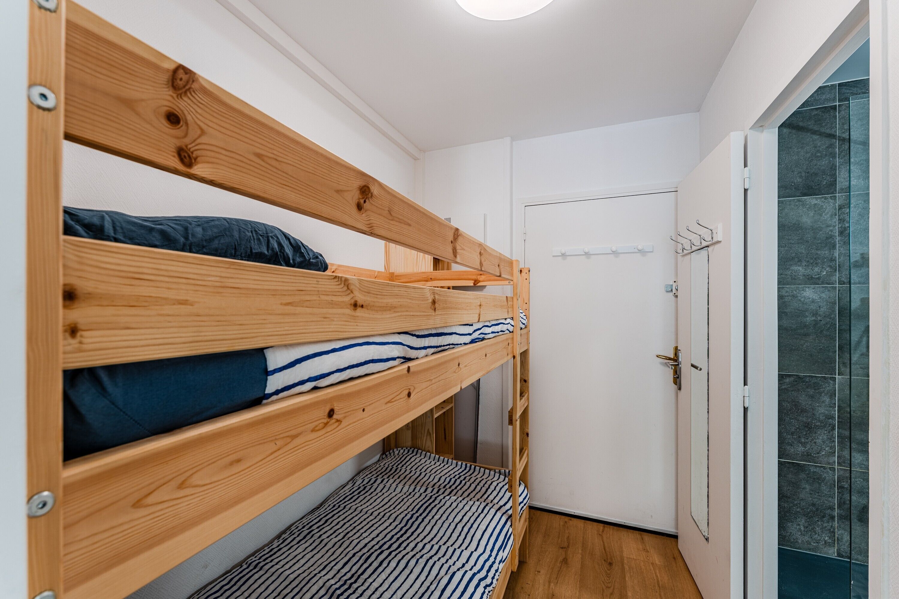 A bunk bed with wooden slats and a striped blanket, a white door, and a tiled wall.