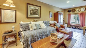 Una habitación acogedora con una cama, una mesa de madera, una silla de mimbre y un ventanal con cortinas.