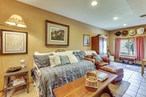 A cozy room with a bed, a wooden table, a wicker chair, and a window with curtains. - Historic Monterey Cabin on 230 Scenic Acres (Monterey)