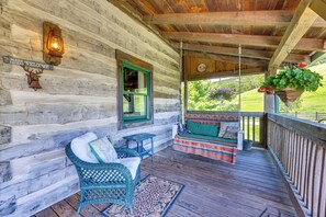 A log cabin with a porch, a wooden bench, a wicker chair, and a hanging planter. - Historic Monterey Cabin on 230 Scenic Acres (Monterey)