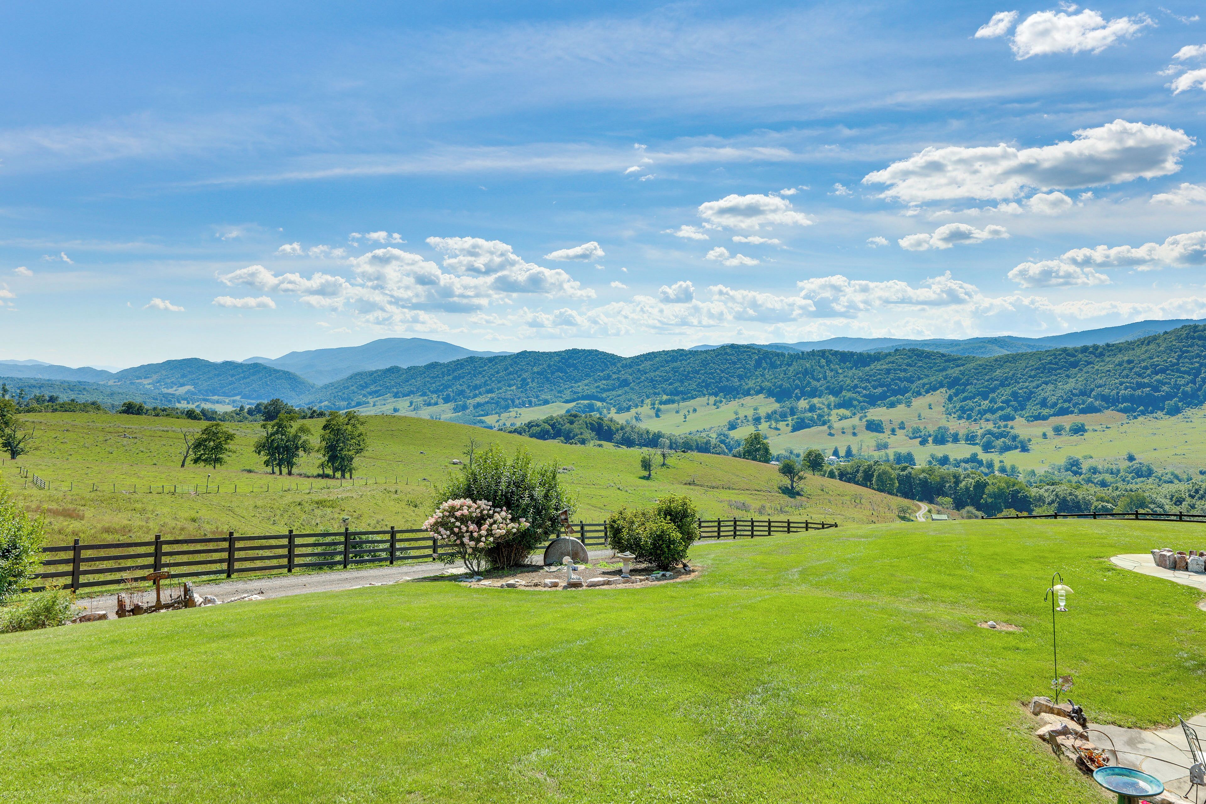 A grassy field with a wooden fence, a small tree, and a distant mountain range under a clear sky.