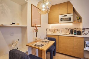 A compact kitchen with wooden cabinets, a built-in microwave, and a dining area with a table set for two. - A charming haven in the heart of Montmartre (Paris)