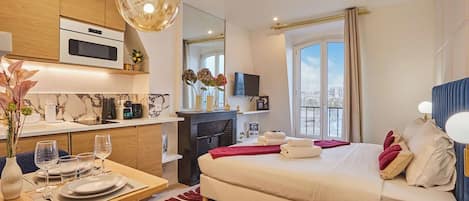A hotel room with a bed, a desk, a dining area, and a large window.