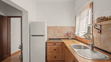 Una cocina compacta con refrigerador, gabinetes de madera, un lavamanos y un ventanal con cortina.