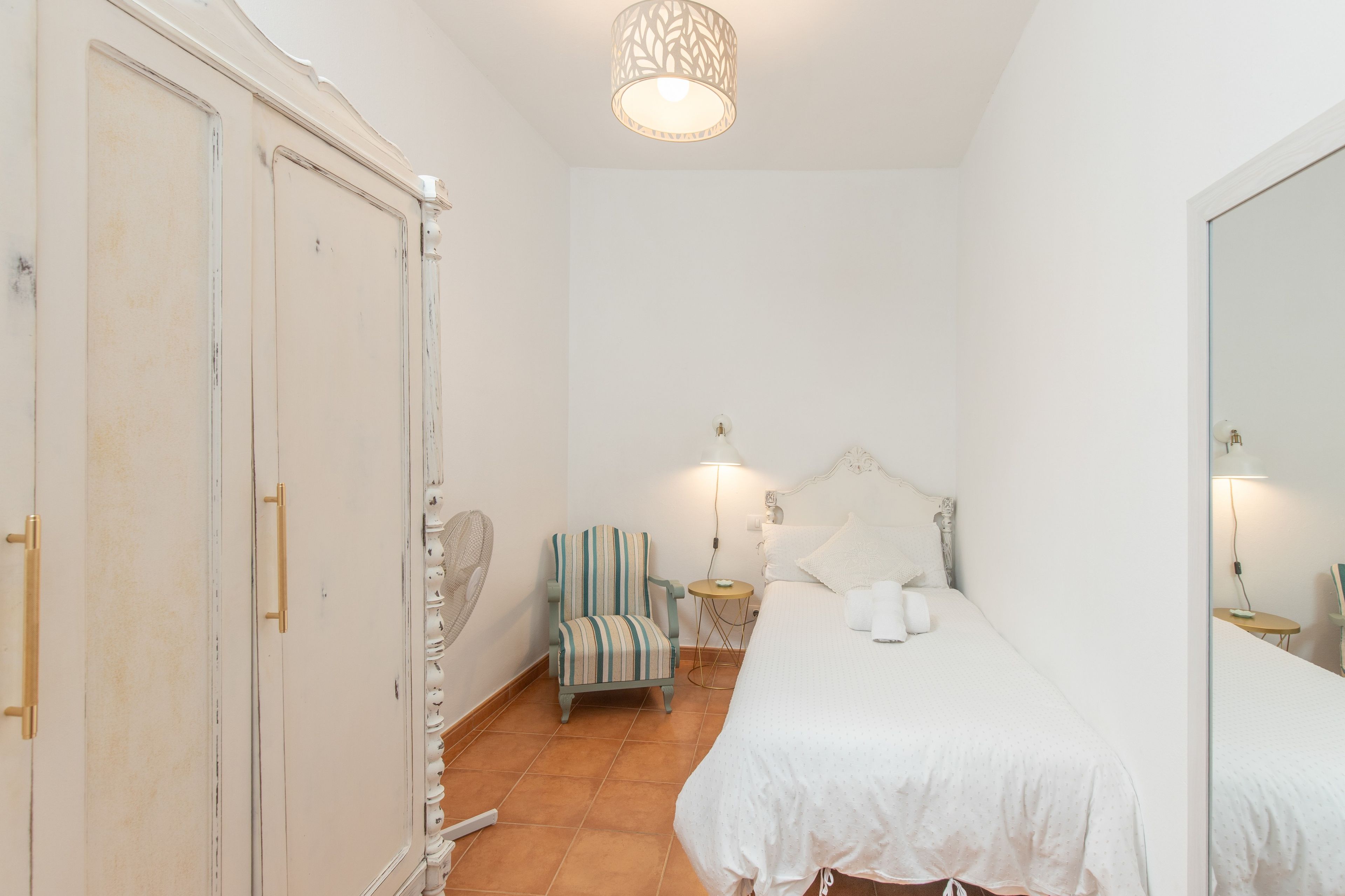 Un dormitorio con cama, una silla, un armario y una lámpara colgante.