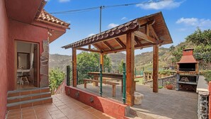 Eine überdachte Terrasse im Freien mit einer Pergola, einem Grill und Blick auf die umliegende Landschaft.