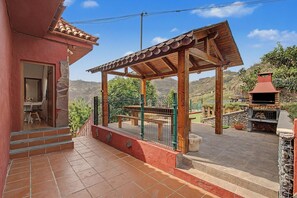 Eine überdachte Terrasse im Freien mit einer Pergola, einem Grill und Blick auf die umliegende Landschaft.