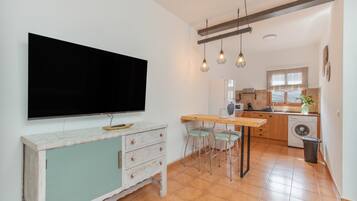 Una cocina moderna con televisor de pantalla plana, lámparas colgantes y un comedor con taburetes de bar.