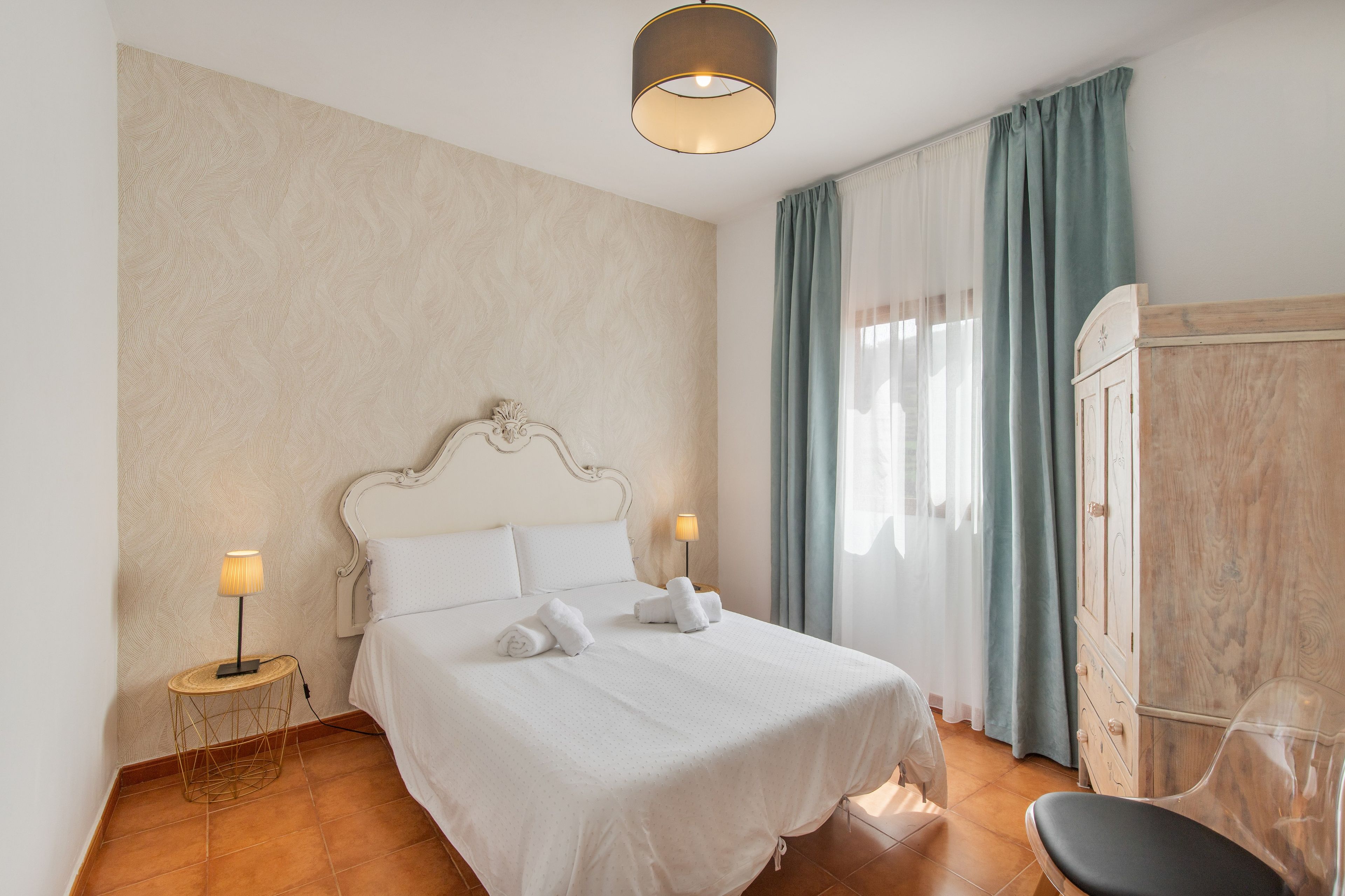 Habitación de hotel con una cama grande, dos lámparas de noche, un armario de madera y una silla.