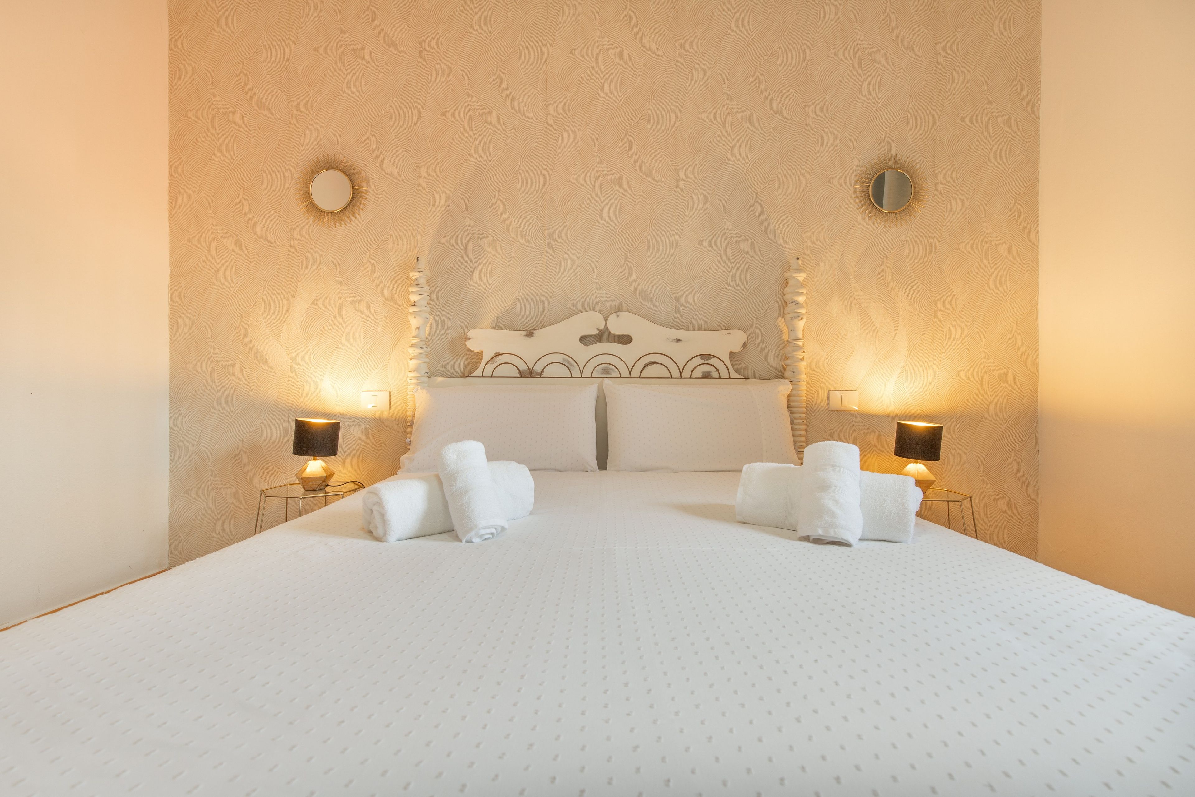 Una habitación de hotel con una cama grande, dos lámparas de noche y un cabecero decorativo.