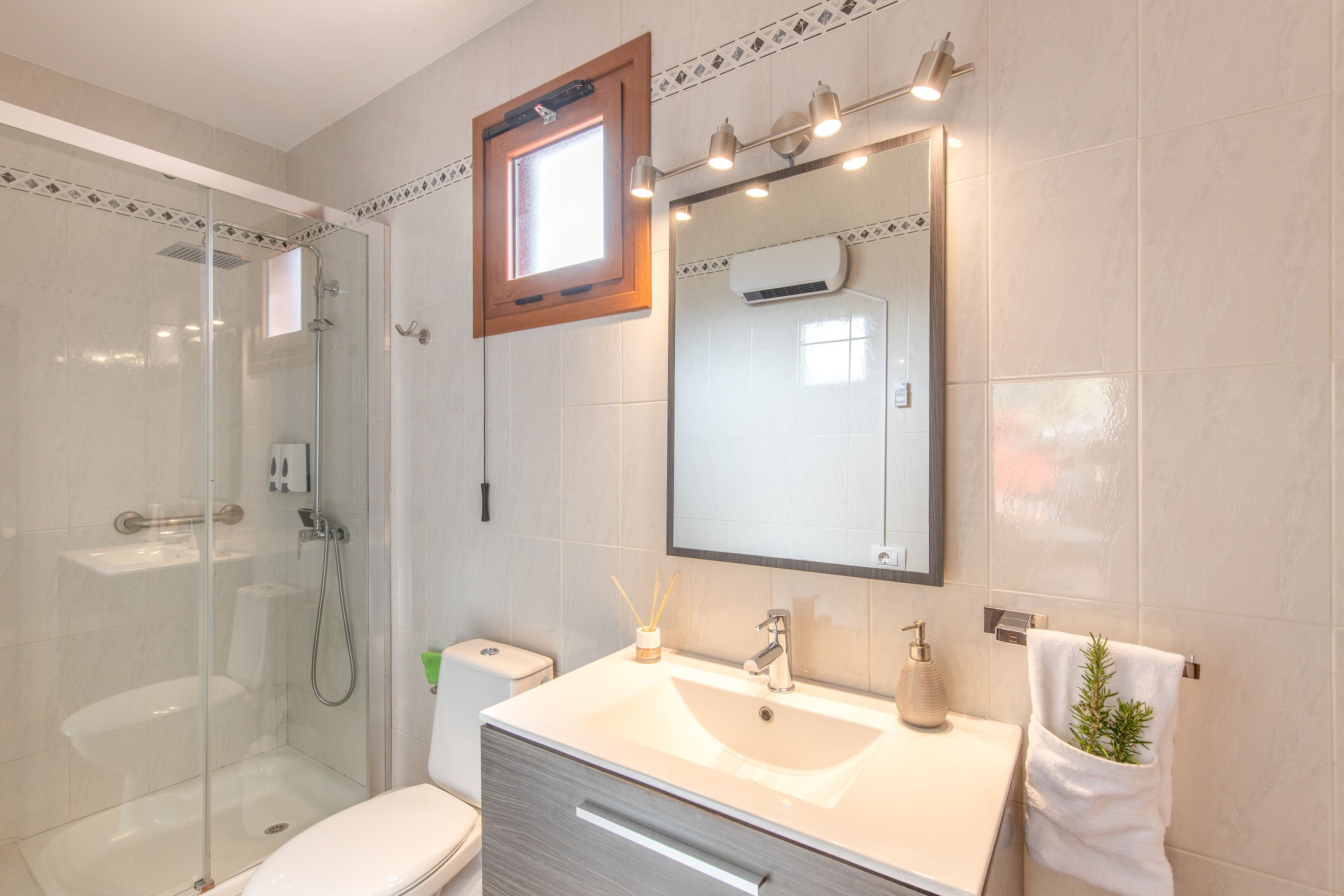 Un baño moderno con ducha envuelta en vidrio, tocador con espejo y un inodoro.