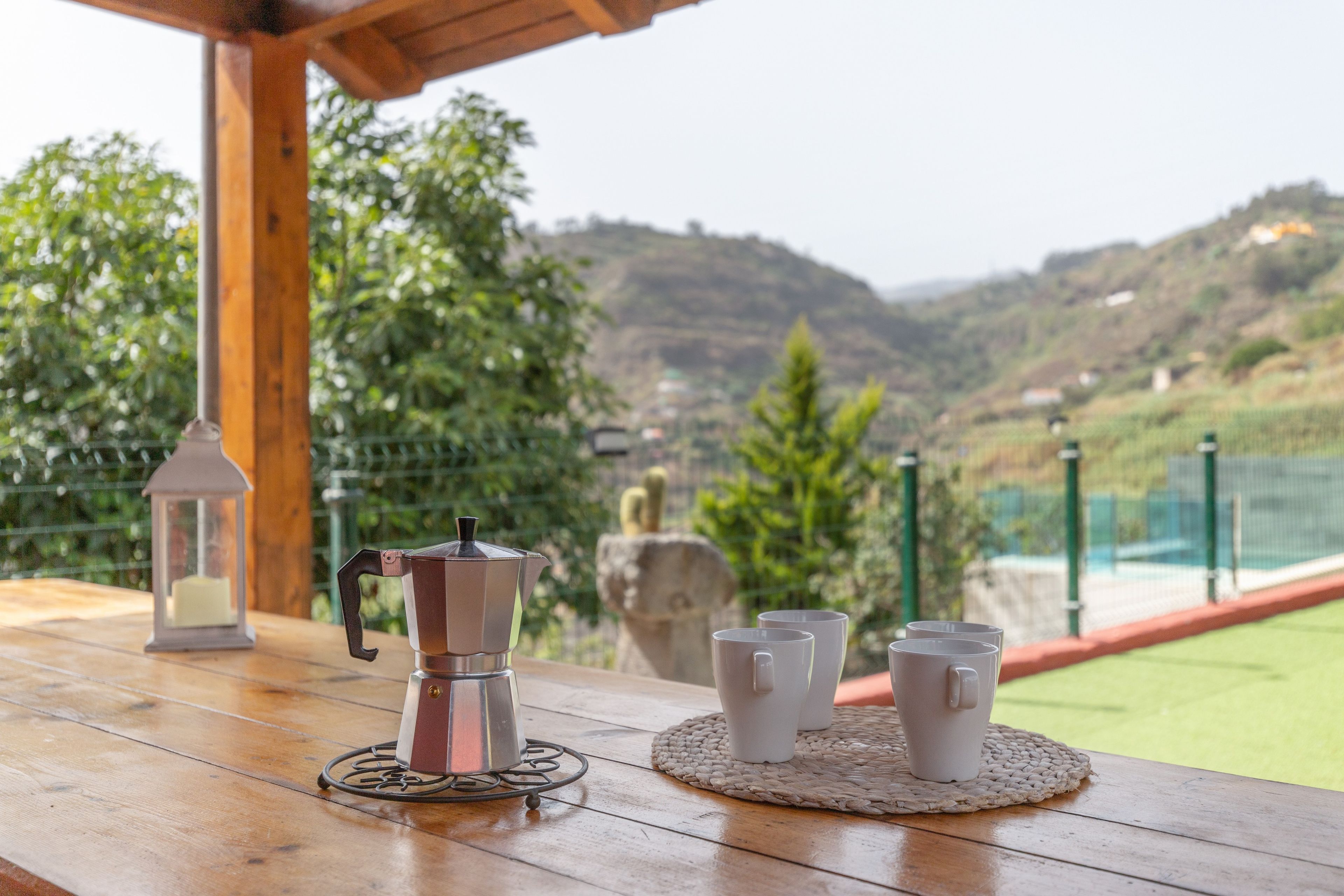 Una mesa de madera con una cafetera, tazas y un farol.