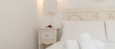 A neatly made bed with folded white towels, a small bedside table with a lamp, and a wall-mounted light fixture.