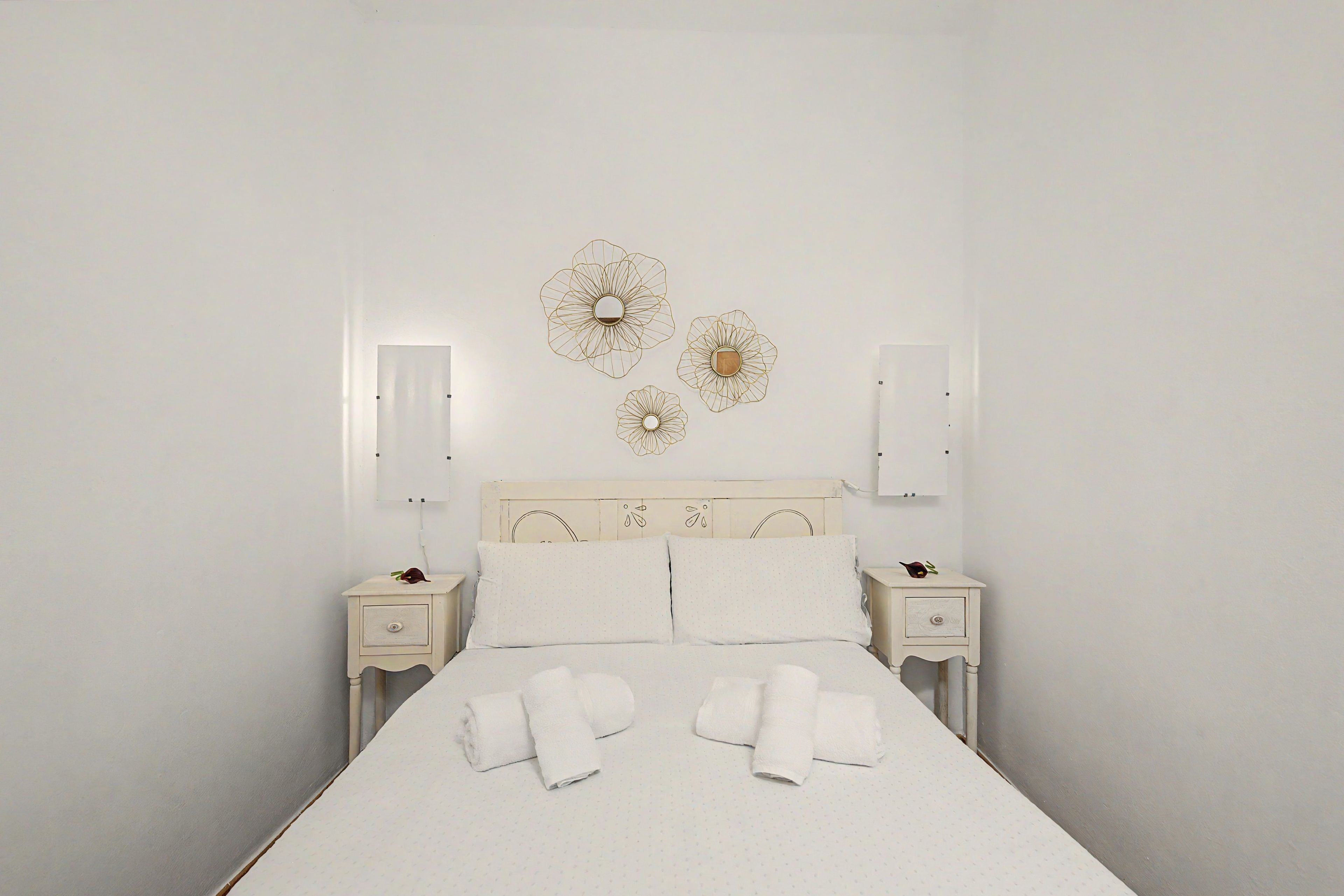 Una cama bien tendida con sábanas y toallas blancas, un cabecero de madera y lámparas fijadas a la pared.
