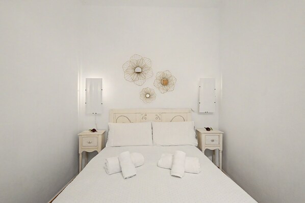 A neatly made bed with white linens and towels, a wooden headboard, and wall-mounted light fixtures.