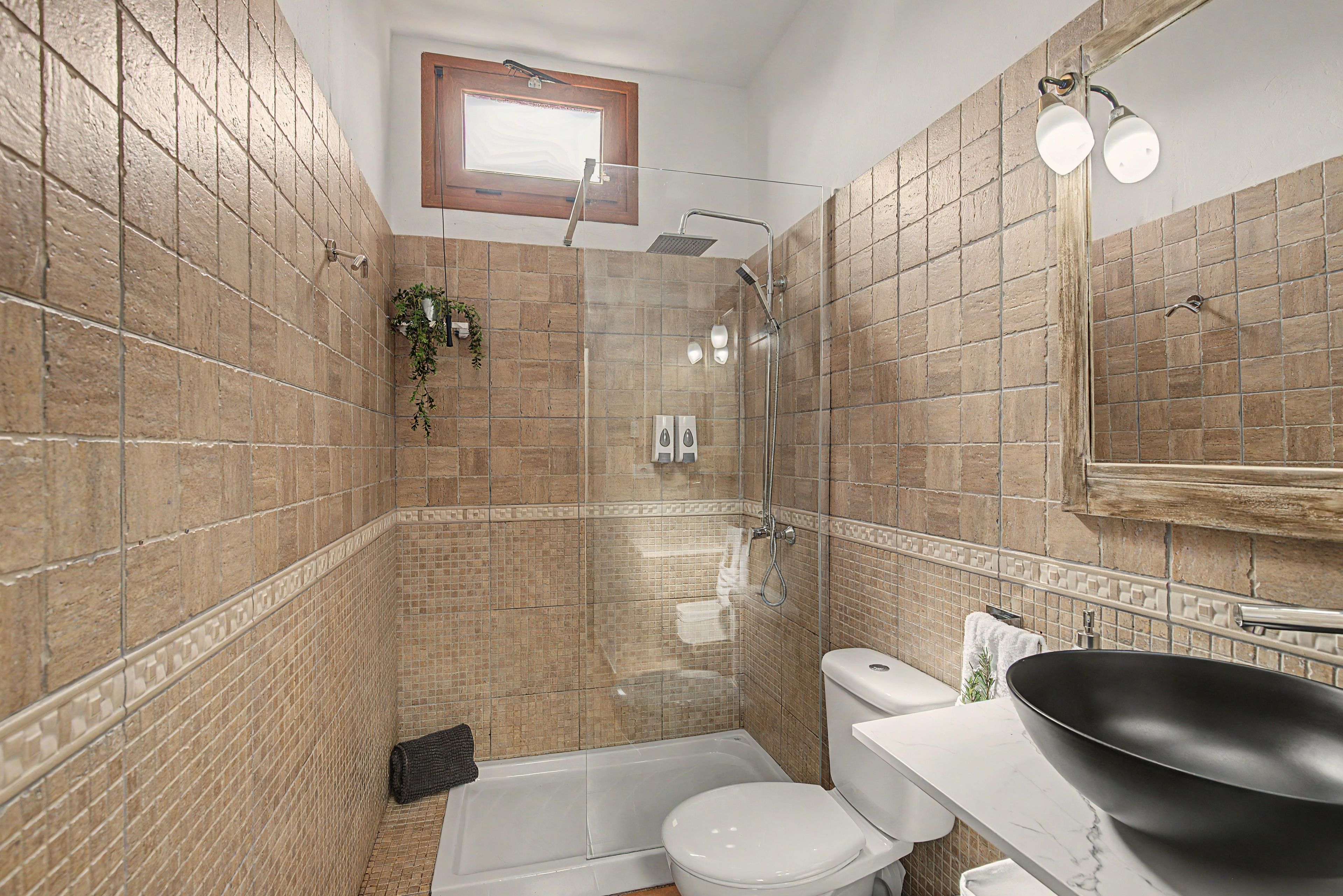 Un baño con ducha, inodoro y lavamanos, con paredes de azulejos y una ventana.
