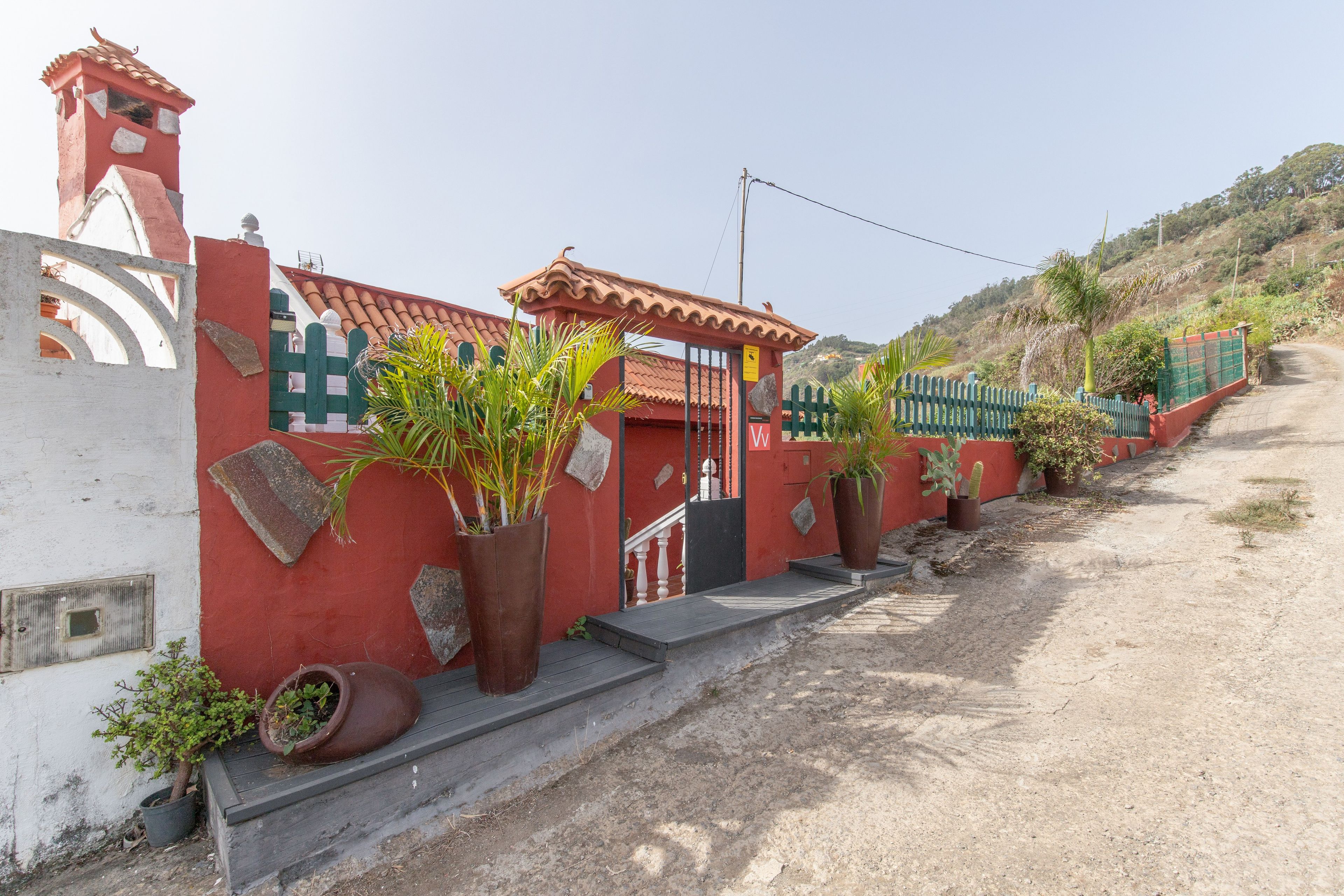 Un edificio rojo y blanco con techo de tejas, una reja y un sendero de tierra que conduce hasta él.