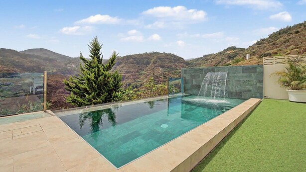 Ein rechteckiger Infinity-Pool mit Wasserfall, umgeben von einer Steinmauer und einer Rasenfläche.
