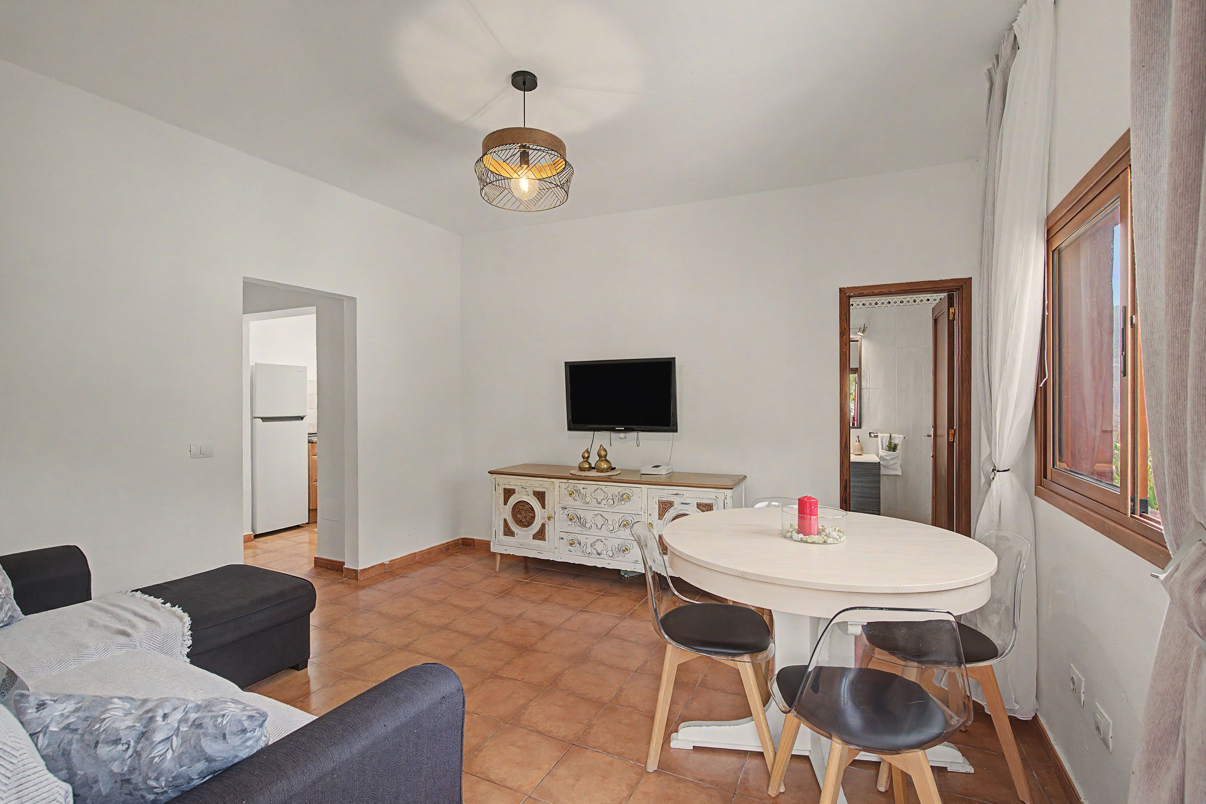 Ein Wohnzimmer mit einer Couch, einem Esstisch mit Stühlen, einem Fernseher und einer dekorativen Lampe.