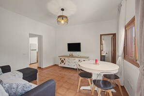 A living room with a sofa, a dining table with chairs, a television, and a decorative light fixture.