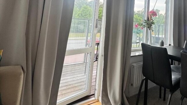 A room with a sliding glass door leading to an outdoor area, a dining table with chairs, and a vase with flowers on the windowsill. - Urban Rest Kalmar City (Kalmar)