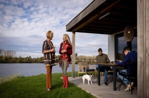An outdoor patio area with a view of a lake, a covered seating area, and a dog. - Premium Water 4p Villa in Thorn (Thorn)