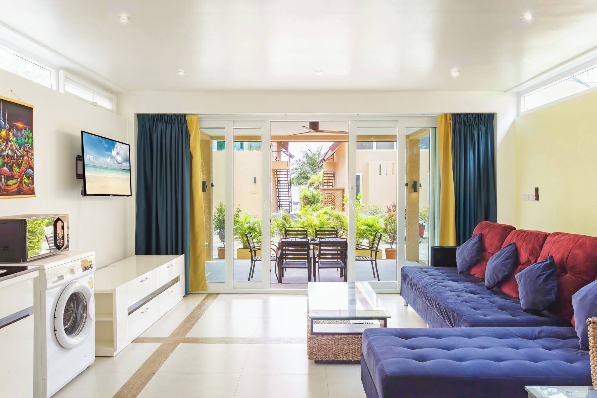 A modern living room with a sofa, a coffee table, a washing machine, and a dining area with chairs and a table.