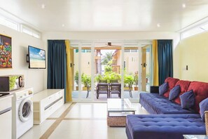 A modern living room with a sofa, a coffee table, a washing machine, and a dining area with chairs and a table.