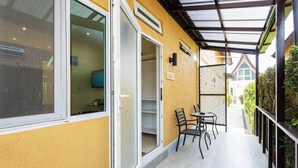 A covered outdoor area with a yellow wall, a sliding glass door, a small table with chairs, and a metal fence. - Beach Villa 21D Blue Haven Bay Resort - 4 Rooms (Ko Chang)