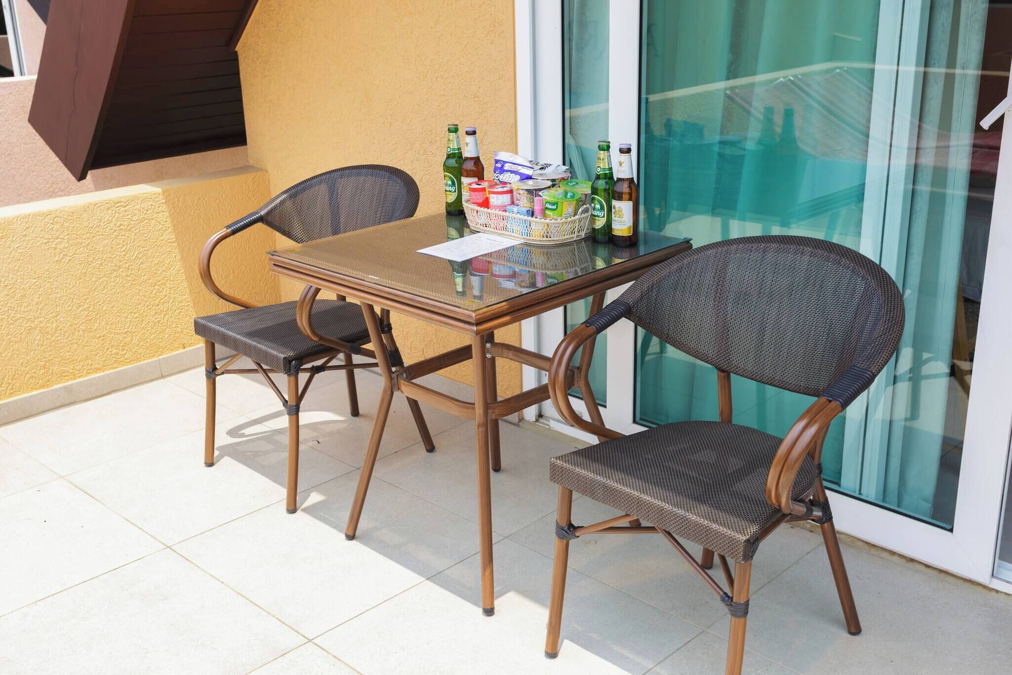 An outdoor patio with a table and two wicker chairs, a glass door, and a window.
