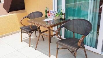 An outdoor patio with a table and two wicker chairs, a glass door, and a window.