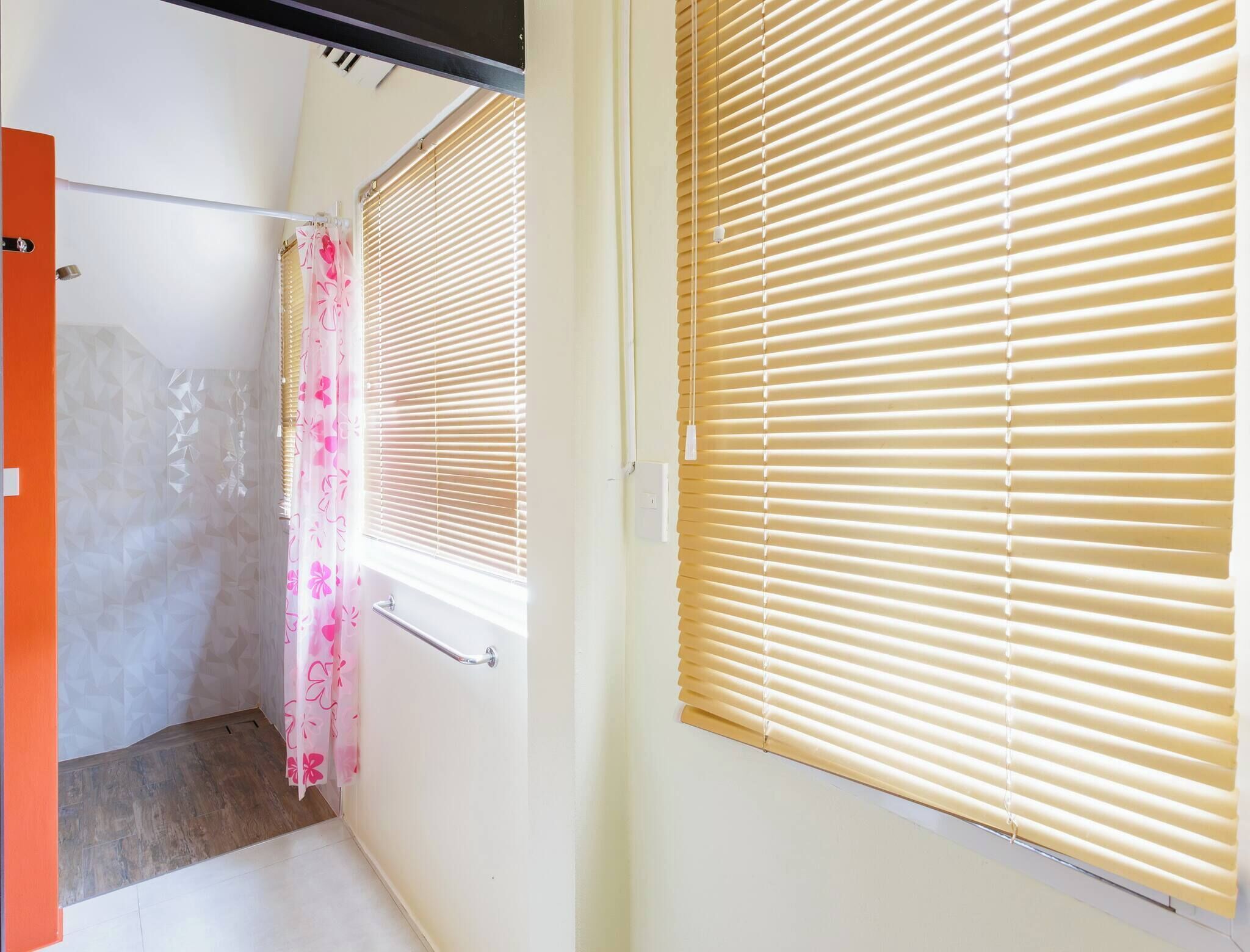 Un couloir étroit avec un espace douche, des toilettes et une fenêtre équipée de stores.