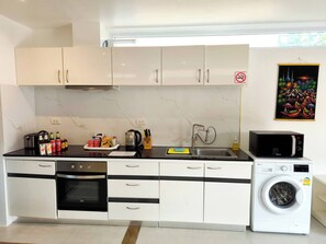 A modern kitchen with white cabinets, a built-in oven, a microwave, and a washing machine.