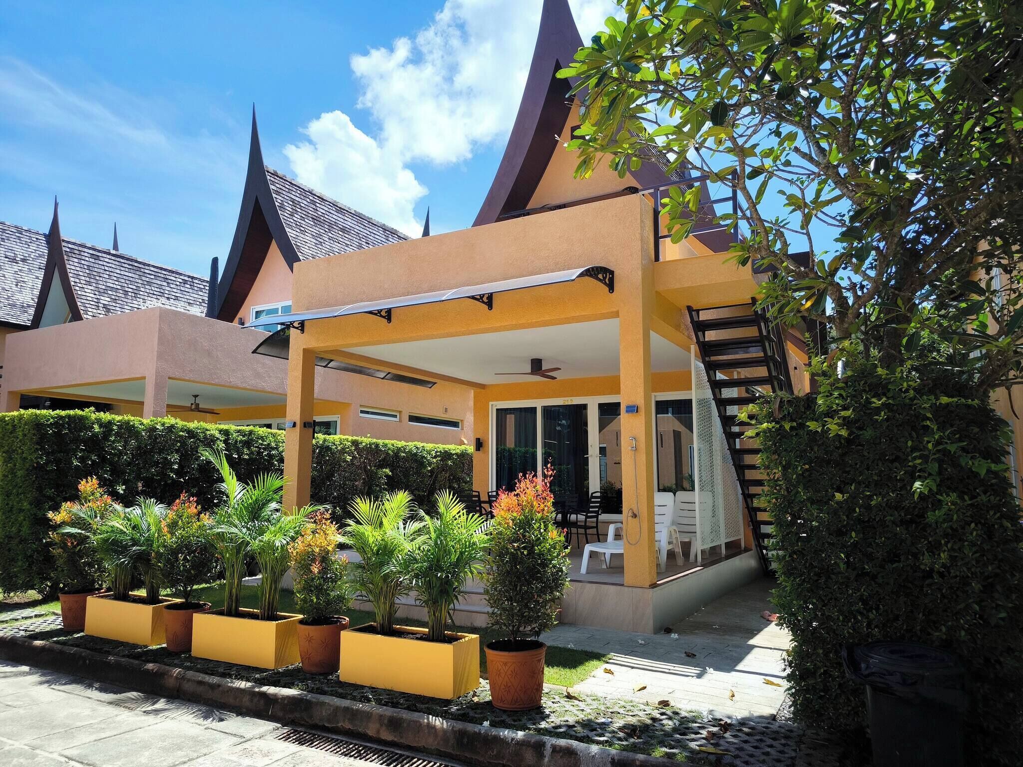 A modern building with a covered outdoor seating area, a staircase, and a well-maintained garden with various plants.