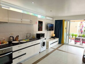 A modern kitchen with a washing machine, a microwave, and a dining area with a table and chairs. - Beach Villa 21D Blue Haven Bay Resort - 4 Rooms (Ko Chang)