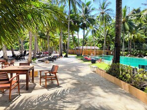 A resort with outdoor seating, a swimming pool, and palm trees.