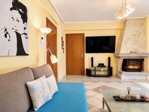 A living room with a sofa, a flat-screen TV, a fireplace, and a wall-mounted artwork. - Athens Skyline - Spacious 3BR for 5 by ΜΡS (Kesariani)