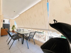 Een balkon met een barbecue, stoelen en een tafel.