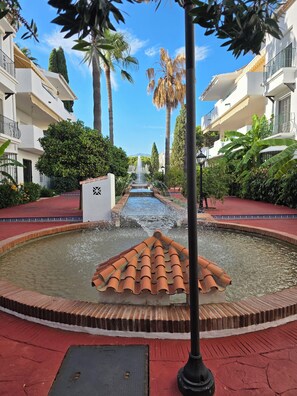 A courtyard with a central fountain, surrounded by palm trees and a red-tiled walkway. - A lovely spacious 2-bed apartment  on beautiful El Presidente Urbanisation, (Estepona)