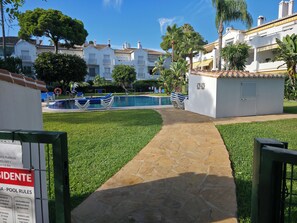 A pool area with a stone pathway, lounge chairs, and a sign indicating pool rules. - A lovely spacious 2-bed apartment  on beautiful El Presidente Urbanisation, (Estepona)